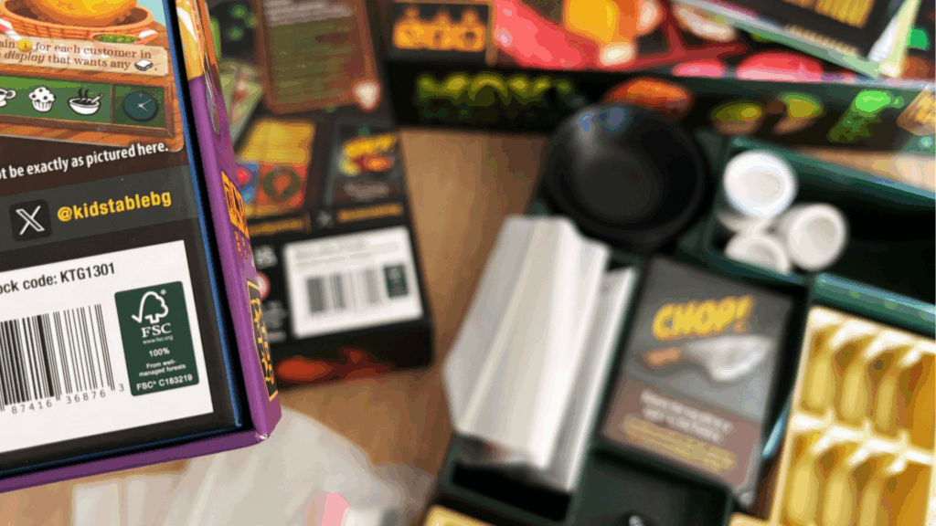 Eco-friendly board game packaging with cardboard inserts and plastic-free paper wrap, shown on a wooden table with game components