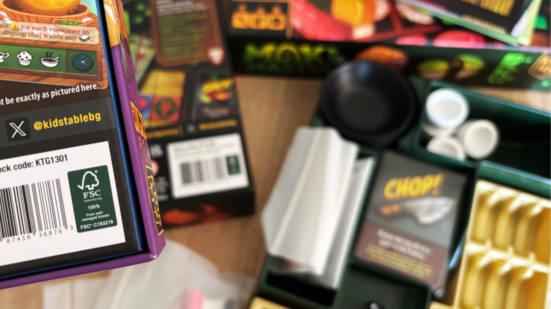 Eco-friendly board game packaging with cardboard inserts and plastic-free paper wrap, shown on a wooden table with game components